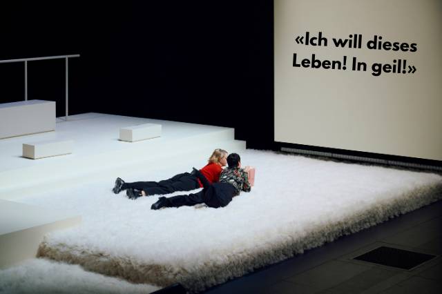 Zwei Personen liegen auf dem Bauch auf einer Matratze und schauen auf eine Leinwand