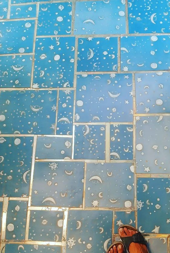 Fußboden mit türkisblauen Keramikfließen. Ein Fuß mit Sandale ist am unteren rechten Bildrand zu erkennen.