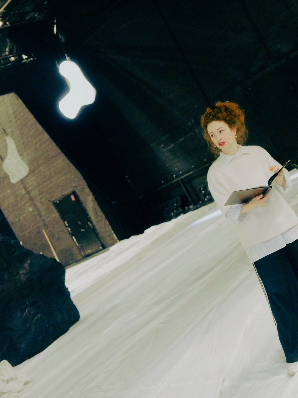 Lea Marlen Balzer mit Regiebuch in der Hand. Sie steht im Bühnenbild bestehend aus einem weißen Tanzboden und schwarzen Felsformationen.