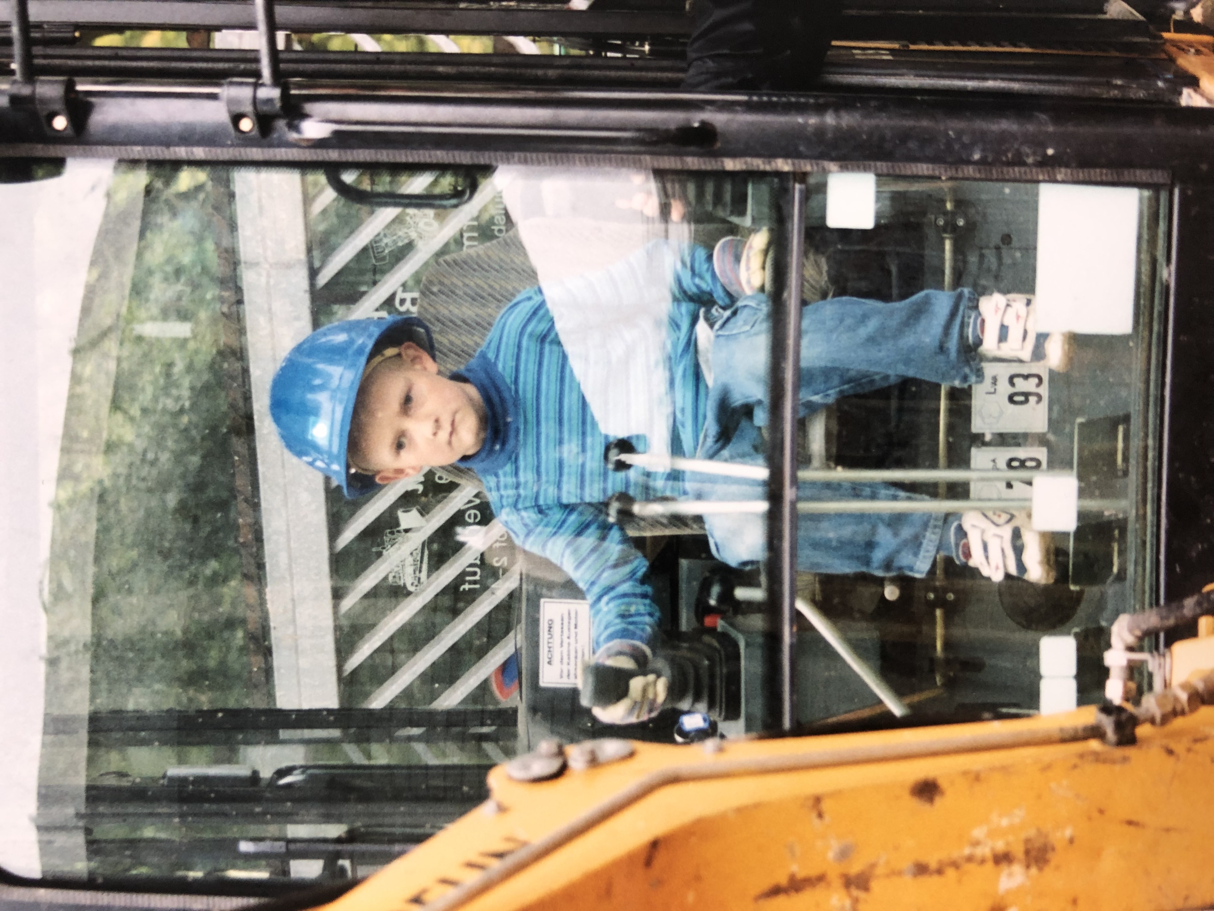 Leo Meier als Kind mit einem blauen Bauarbeiterhelm auf einem gelben Bagger